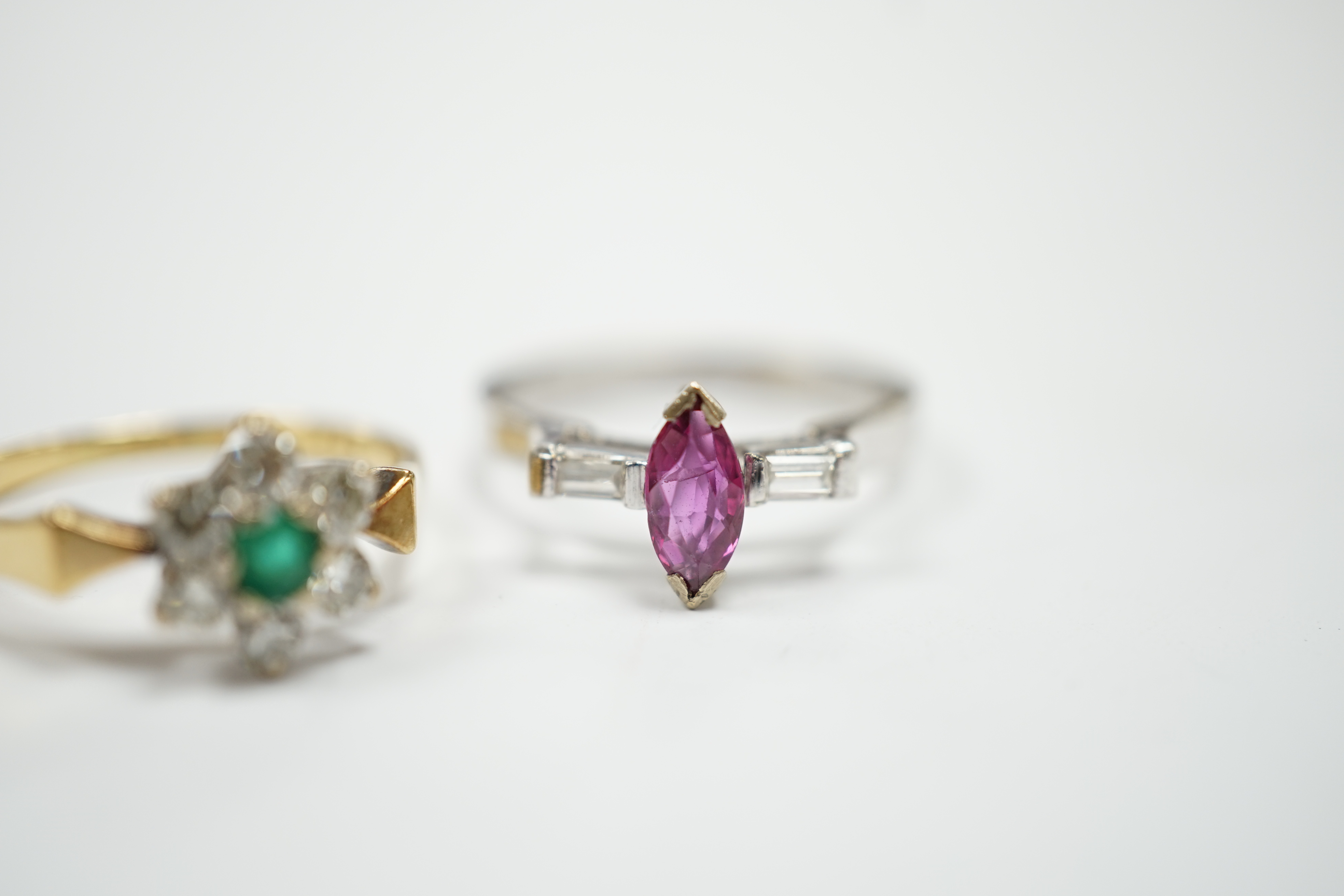 An 18ct, emerald and diamond set flower head cluster ring, size N and an 18ct white metal ruby and diamond set three stone ring, size L/M, gross weight 6.2 grams.
